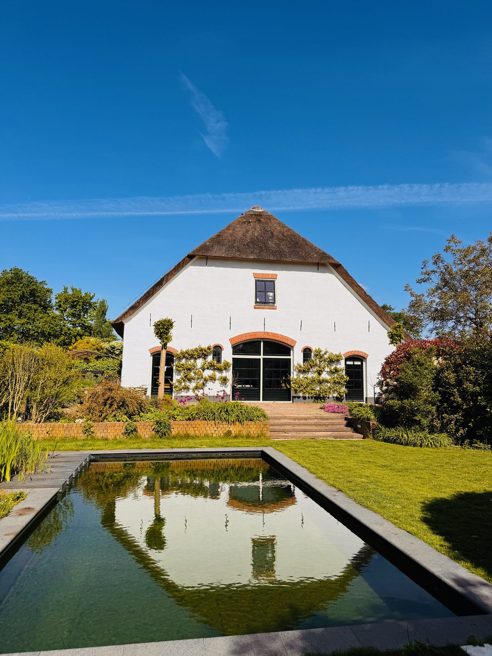 Brede tuin met spiegelvijver en rietgedekt huis